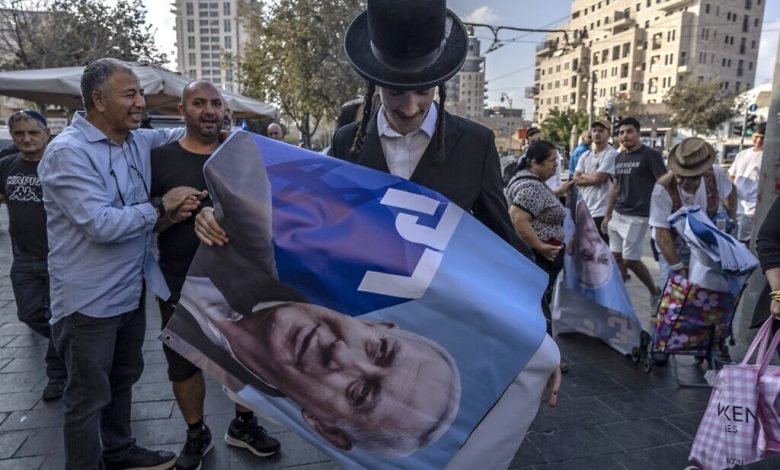 رجل يهودي متشدجد يحمل ملصقًا يحمل صورة رئيس الوزراء السابق وزعيم حزب الليكود بنيامين نتنياهو، خلال تجمع انتخابي لحزب الليكود في سوق محانيه يهودا في القدس، قبل الانتخابات العامة في نوفمبر، 20 أكتوبر 2022 (MENAHEM KAHANA / AFP)