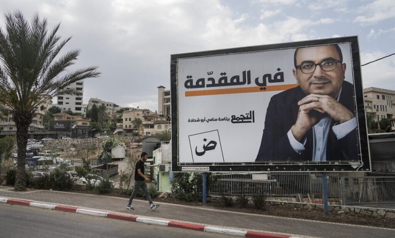 رجل يمر من أمام لوحة إعلانية لحملة انتخابية تحمل صورة سامي أبو شحادة، رئيس حزب التجمع الوطني، في مدينة أم الفحم شمال إسرائيل، الجمعة 21 أكتوبر، 2022. (AP / Mahmoud Elean)